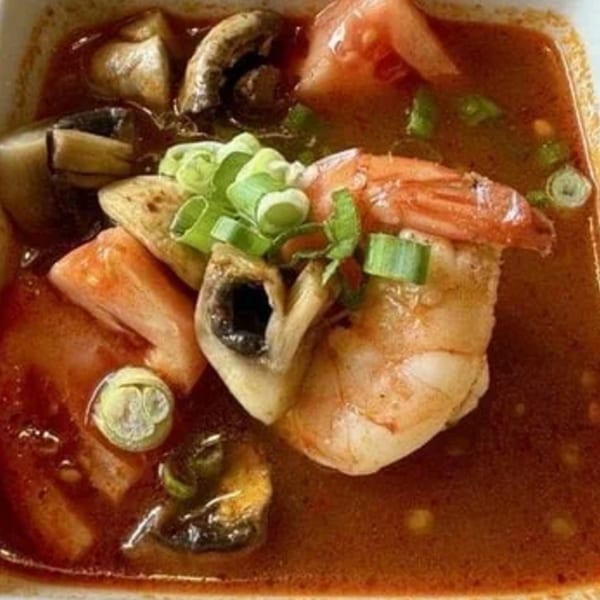 Close-up of Thai Tom Yum soup with shrimp, mushrooms, tomatoes, and green onions.