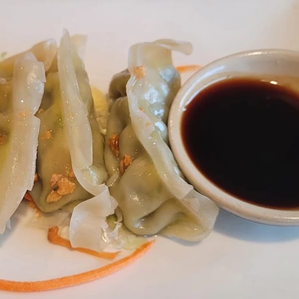 Steamed Thai dumplings with crispy garlic and a side of soy sauce on a white plate.