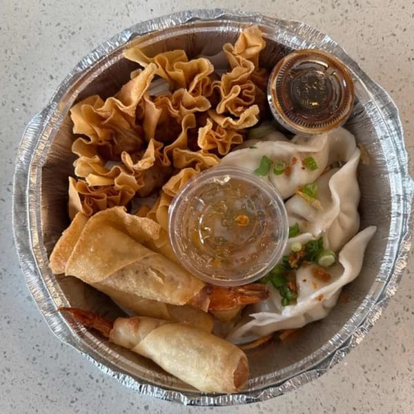 A Thai appetizer platter in a foil container with fried wontons, spring rolls, dumplings, and dipping sauces.